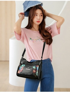 Detail view of printed soft leather crossbody bag with multiple zippers shown on a model