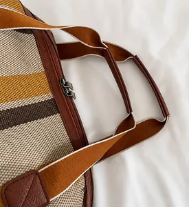 Detailweergave van gestreepte canvas tas met bruine lederen handvatten en dubbele rits