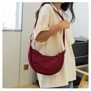 Detail showing the deep red nylon crescent bag worn crossbody with adjustable strap