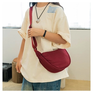 Detail of burgundy crescent nylon crossbody bag showing pleated texture and wide strap