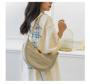 Close-up of lightweight beige nylon crescent bag worn on a model in a minimalist setting