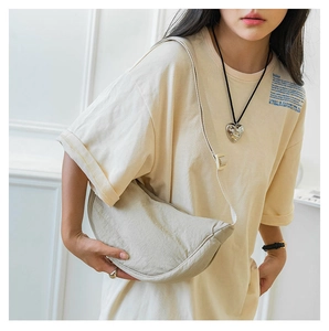 Detail of a beige nylon crescent crossbody bag with minimalist pleated texture and strap