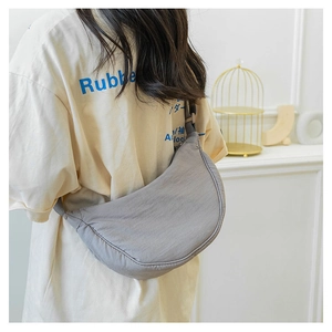 Gray nylon half-moon crossbody bag shown on model in a minimalist home setting