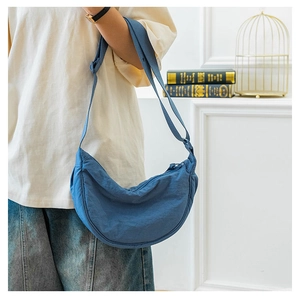 Blue nylon crescent bag with adjustable strap and textured surface on a lifestyle model