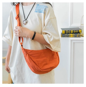 Detail of adjustable strap and orange nylon crescent bag on a model in white tee