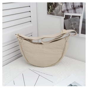 Beige crescent moon shoulder bag with adjustable strap on a minimalist white countertop
