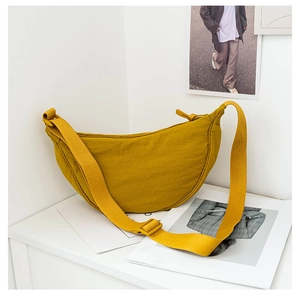 Detailed close-up of a mustard yellow crescent nylon crossbody bag on a clean white desk