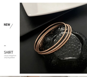 Detailed view of rose gold titanium steel interlocking bangles set on black texture