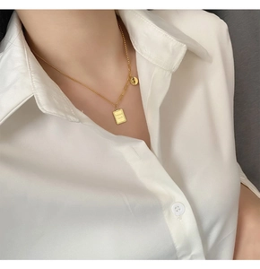 Detail of gold titanium steel necklace with rectangular 'good luck' pendant on white shirt