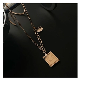 Detail of rose gold titanium necklace featuring Good Luck tag and layered paperclip chain