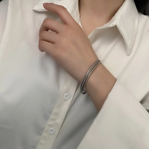 Minimalist silver multi-layered interlocking bangles worn on wrist with white shirt background
