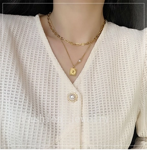 Detail of layered gold titanium necklace featuring a portrait pendant and a white pearl