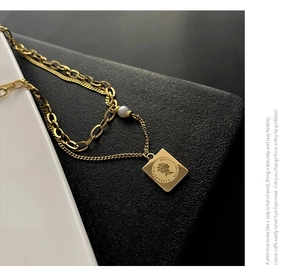Close-up of gold layered chain necklace featuring a pearl and Queen Elizabeth square pendant