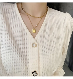 Detail of layered gold titanium necklace featuring a queen portrait coin and white pearl