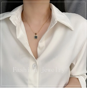 Detail view of a gold geometric square pendant on a delicate chain worn on the neck