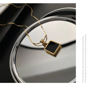 Detailed view of square gold-toned necklace with black enamel inlay on reflective disk