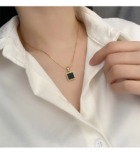 Detail of a gold titanium steel necklace with a square black agate pendant on a model