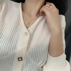 Collier goutte de lave dorée et bague assortie portés sur cardigan blanc élégant