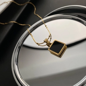 Minimalist gold beaded necklace with a square black onyx pendant on a dark leather surface