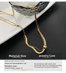 Detail of a double-layered gold snake chain necklace with a polished bead in titanium steel