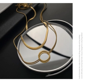 Vue détaillée du collier à double pendentif doré sur un miroir réfléchissant