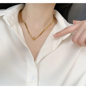Close-up of a gold snake chain necklace with a minimalist polished bead on a model