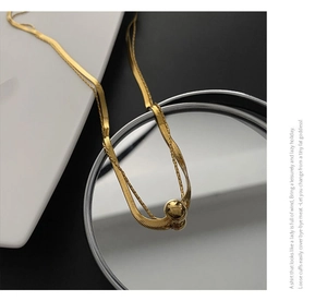 Macro view of golden double-layer snake chain necklace with round bead pendant