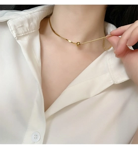 Close-up of a minimalist gold choker necklace featuring a polished round bead on a fine chain