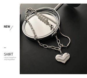 Detail of a dual-layer silver necklace featuring a polished heart pendant and white pearls