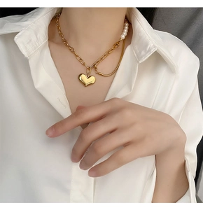 Detail of gold heart pendant with asymmetrical pearl chain on white shirt model