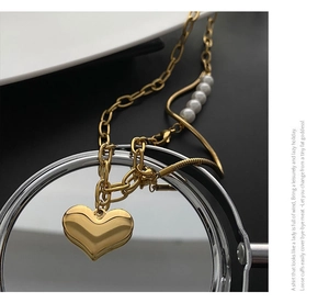Detail of gold 3D heart pendant necklace with pearl and mixed chain link design