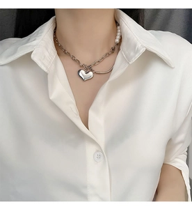 Macro shot of asymmetric chain necklace with pearls and mirrored heart pendant detail