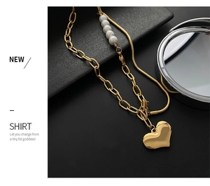 Detail of gold heart pendant necklace with pearls and double chain layers on black surface