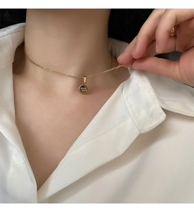 Primo piano di una collana dorata con ciondolo rotondo inciso Good Luck su una modella