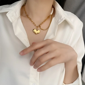 Double-layered gold necklace featuring a polished heart pendant and pearl accents on the neck