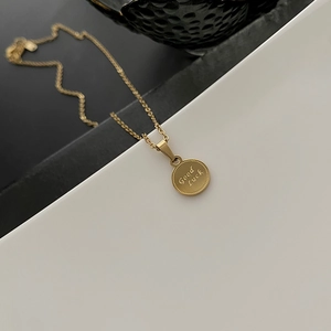 Collana con moneta d'oro minimalista con incisione Good Luck su sfondo a contrasto