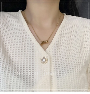 Gros plan détaillé d'un collier doré à pendentif spirale porté sur un haut blanc gaufré