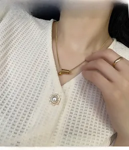 Détail du collier spirale doré et d'une bague polie portés sur un haut texturé