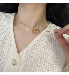 Gros plan d'un collier avec pendentif spirale dorée porté sur un gilet blanc