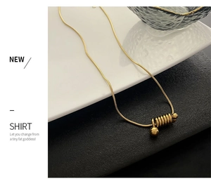 Détail d'un collier chaîne serpent dorée avec pendentif spirale sur assiette