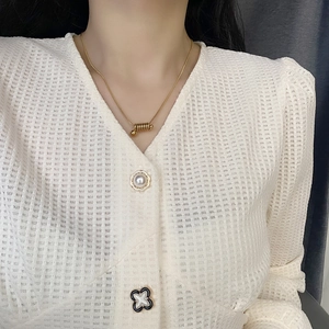 Collier élégant en spirale d'acier titane doré porté sur gilet gaufré beige