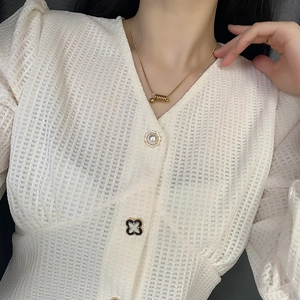 Gros plan d'une femme portant un collier à pendentif spirale doré et un haut en maille blanc