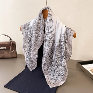 Elegant floral print silk scarf with black scroll patterns hanging on a wooden hanger