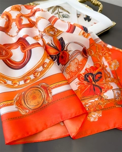 Detail of luxury silk scarf with orange chain print and satin texture on a tray