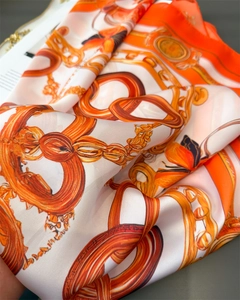 Detailed view of luxury silk scarf with golden chain print and soft orange fabric folds