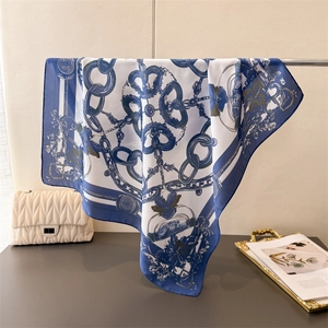 Detail of blue and white silk scarf with chain print draped by a designer handbag