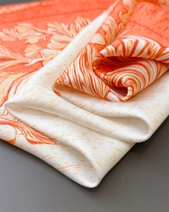 Detail of silk-like floral scarf fabric showing orange flower pattern and soft texture