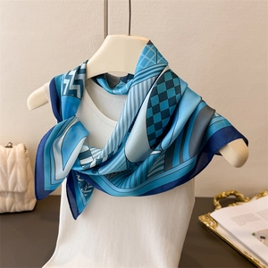 Detailed close-up of blue geometric silk scarf tied elegantly on a white mannequin stand