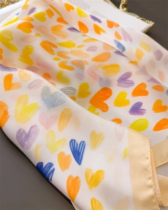 Detailaufnahme des Seidenschals mit bunten Herzmustern und champagnerfarbenem Saum