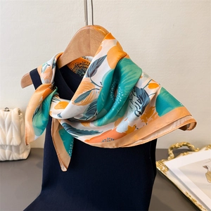 Détail d'un foulard en soie à fleurs oranges et vertes sur un haut en tricot